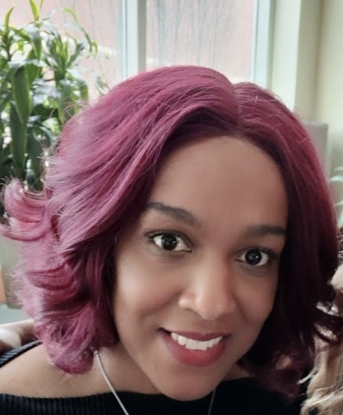 Kirstie smiling, with softly curled burgundy hair